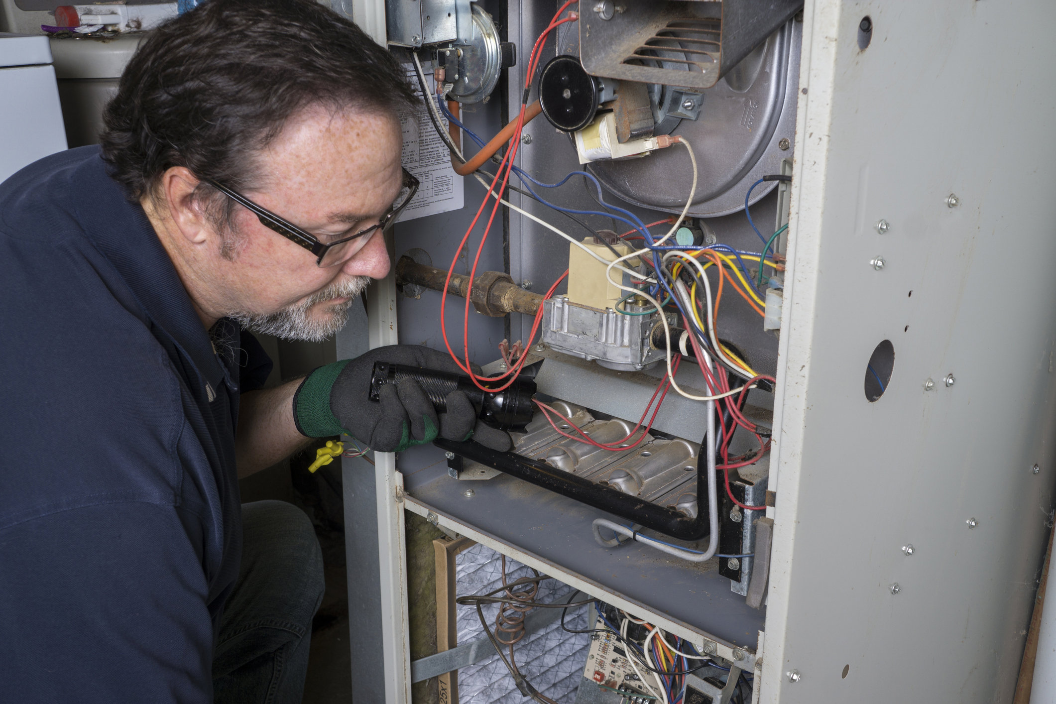 Technician performing furnace repair, inspecting internal components and wiring for efficient heating solutions in Western New York.